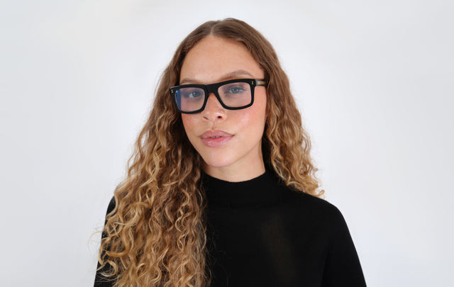 Brunette model with ombré curls wearing Catania Optical in Black/Gold