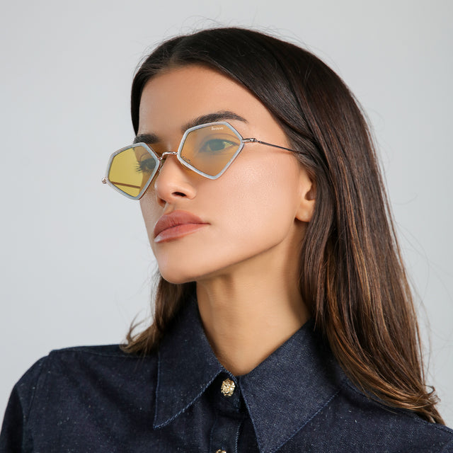Angled portrait of brunette model in a denim blouse wearing Beak Ace 53 Sunglasses Celeste/Rose Gold with Honey Flat See Through