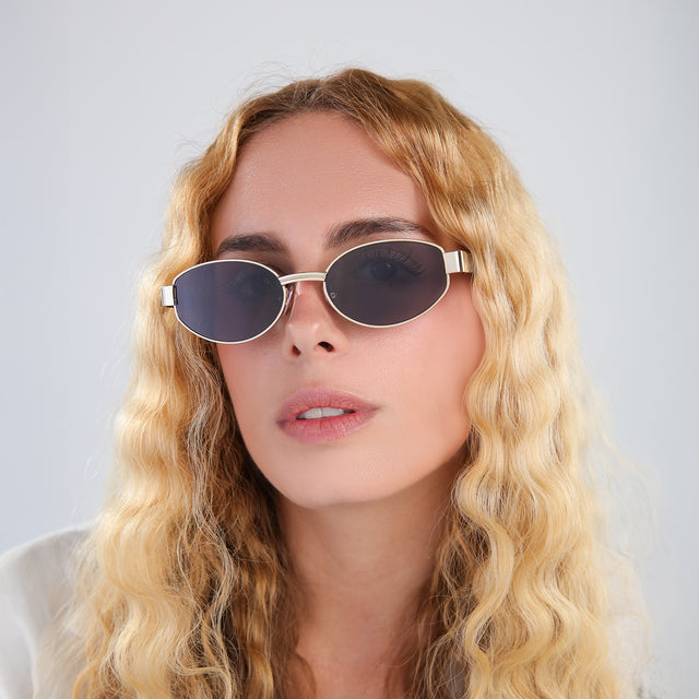 Blond woman with wavy hair in a white linen blouse wearing Bellagio A Sunglasses Gold/Havana with Grey