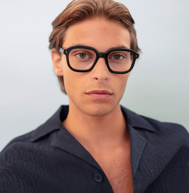 Model with short brown hair in a black linen shirt wearing Bogota Optical Black Optical