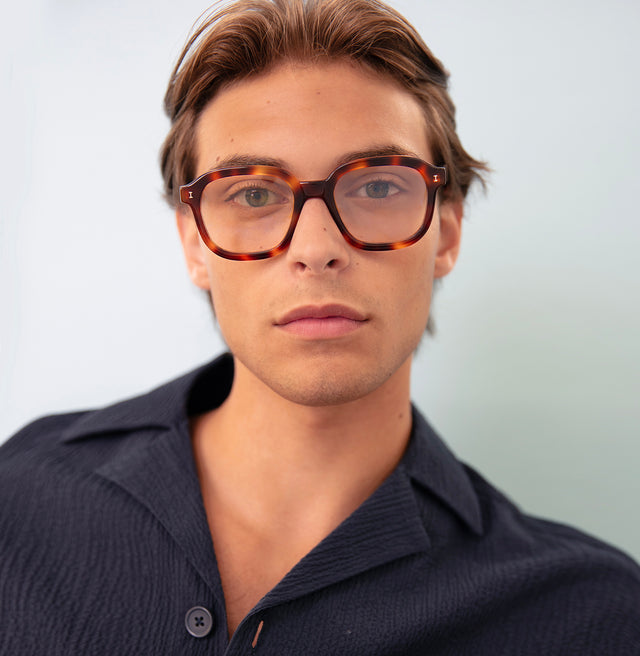 Model with short brown hair in a black linen shirt  wearing Bogota Optical Havana Optical