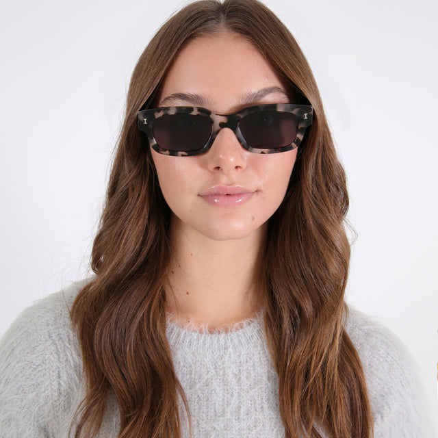 Brunette model with loose curls wearing Cali Sunglasses White Tortoise with Grey
