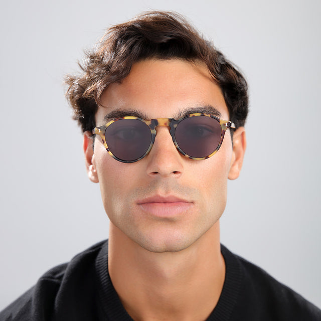 Man with brown hair in a black tee wearing Capri Sunglasses Tortoise with Grey