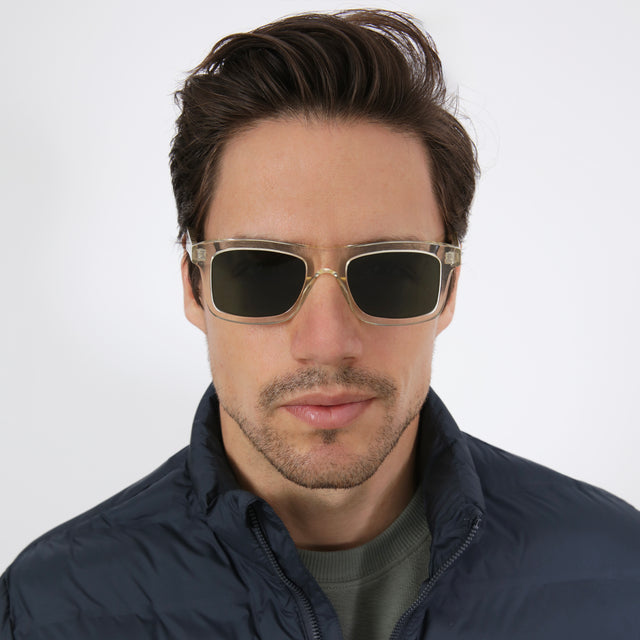 Model with short brown hair in a navy puffer coat wearing Catania Sunglasses Champagne with Olive Flat