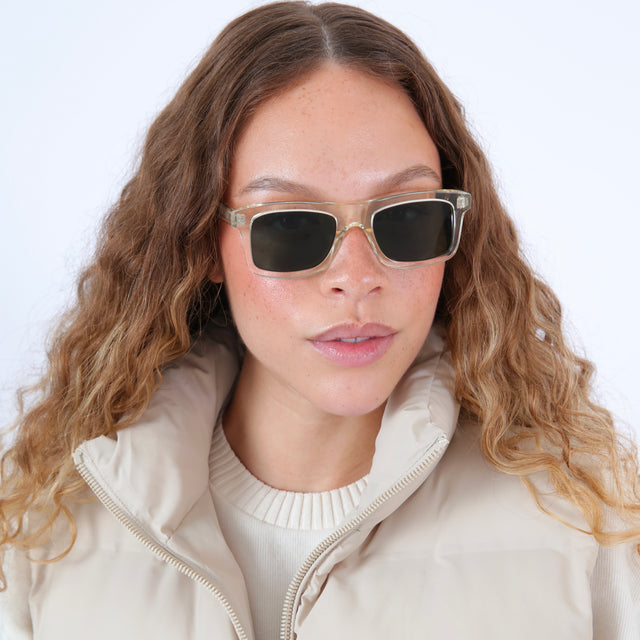 Brunette model with wavy hair in a white puffer jacket wearing Catania Sunglasses Champagne with Olive Flat