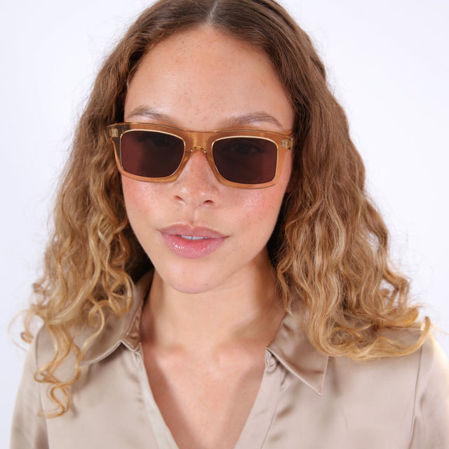 Brunette model with wavy hair in a beige silky blouse wearing Catania Sunglasses Citrine with Brown Flat