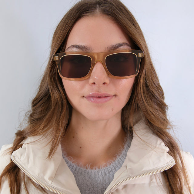 Brunette model in a white puffer jacket wearing Catania Sunglasses Citrine with Brown Flat