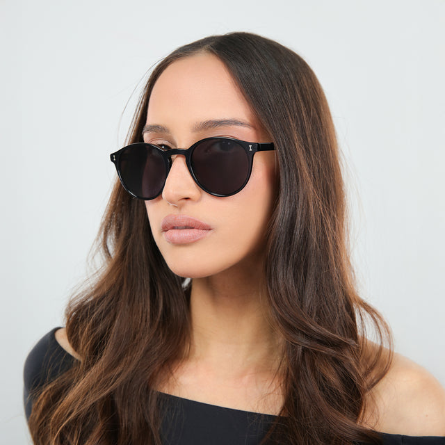 Another angle of brunette woman in an off-the-shoulder blouse wearing Como Sunglasses Black with Grey