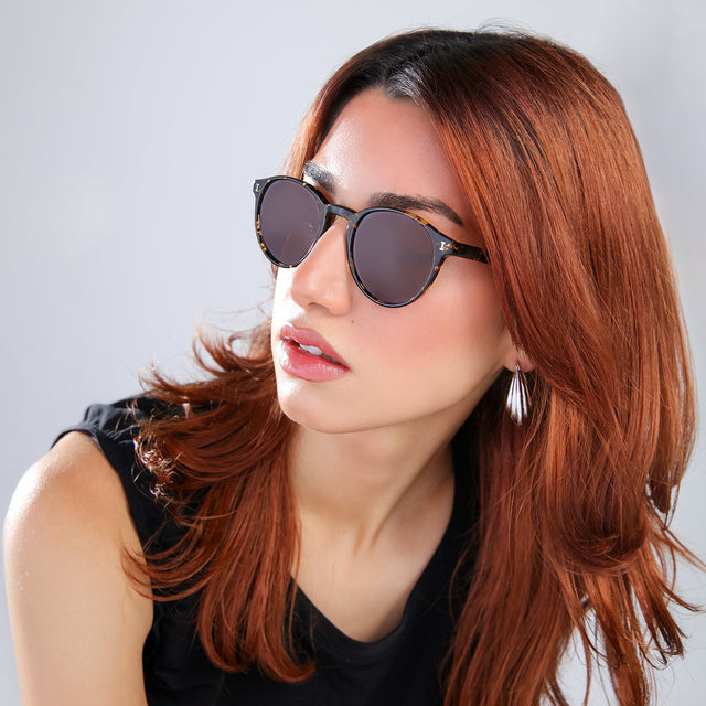 Close up of woman with red hair in a black blouse looking right Como Sunglasses side view in Flame / Brown