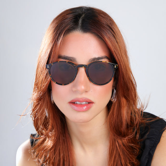 Woman with red hair in a black blouse Como Sunglasses side view in Flame / Brown