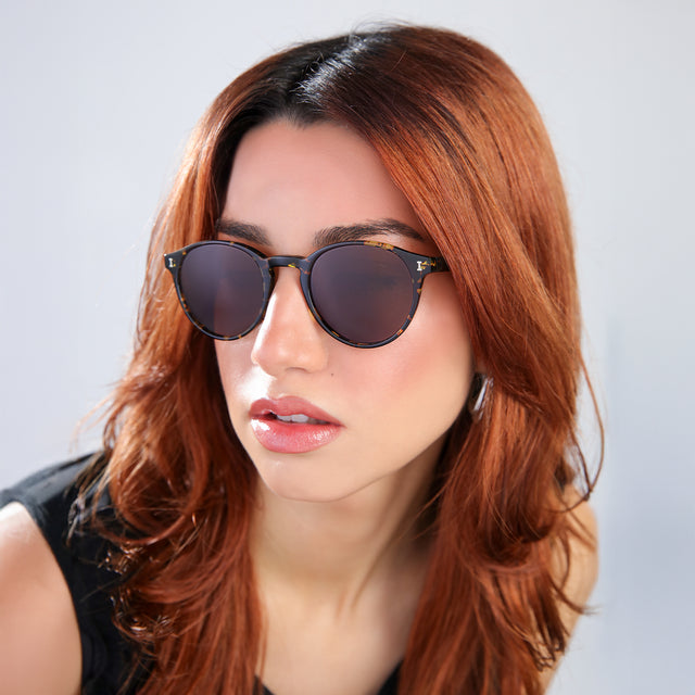 Another angle of woman with red hair in a black blouse Como Sunglasses side view in Flame / Brown
