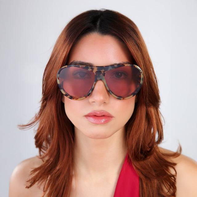Another angle of woman with red hair in a red vest wearing Cynthia Rowley x illesteva Tortoise with Bordeaux See Through