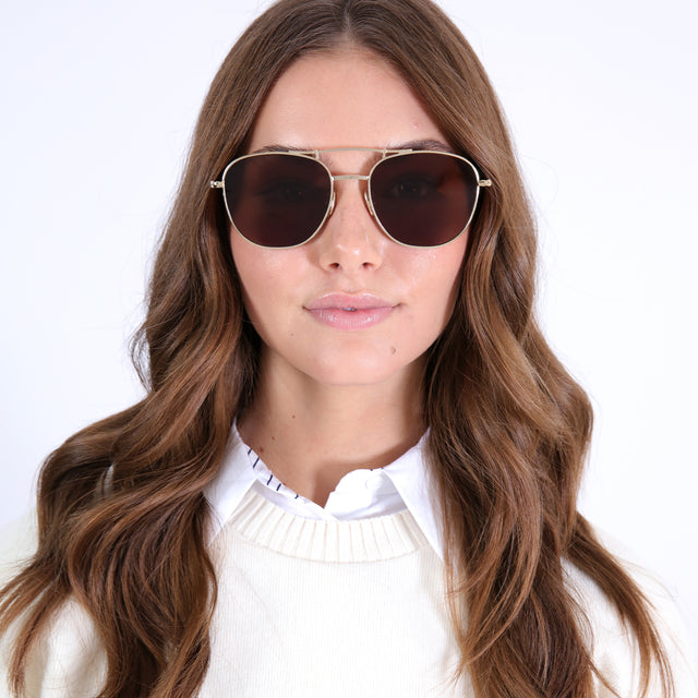 Brunette model with loose curls  wearing Cyprus Sunglasses Gold with Brown Flat