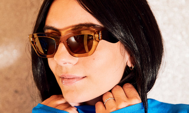 Model with sleek black hair in an electric blue shirt wearing nk x illesteva Donna Sunglasses Cider/Black with Brown