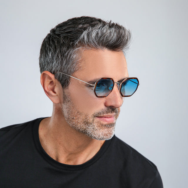 Model with salt and pepper hair and beard in a black shirt looking to his left wearing Dylan Tate Sunglasses Havana/Gold with Blue Flat Gradient See Through