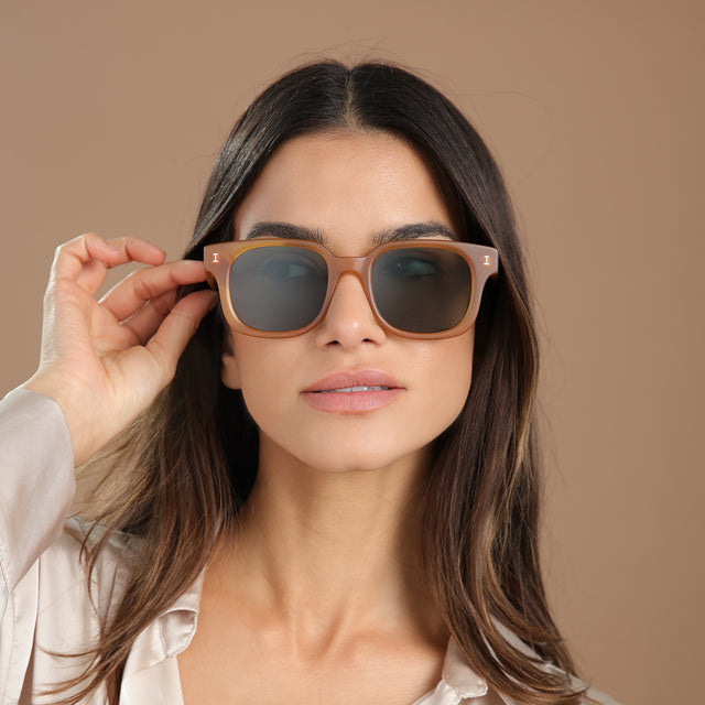 Brunette model in a cream silk blouse wearing Ellison Sunglasses Matte Honey with Olive Flat