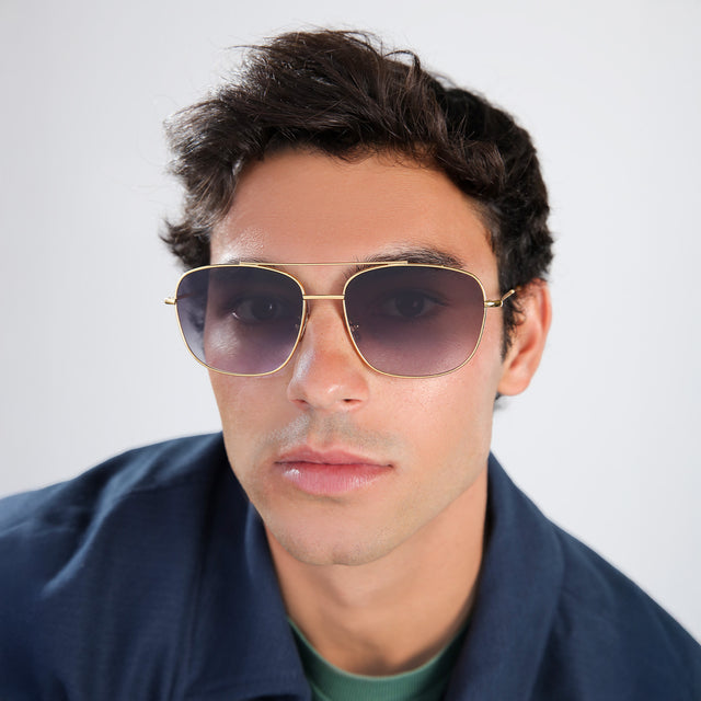Man with brown hair in a navy blue jacket wearing Frankie Sunglasses Gold with Grey Flat Gradient
