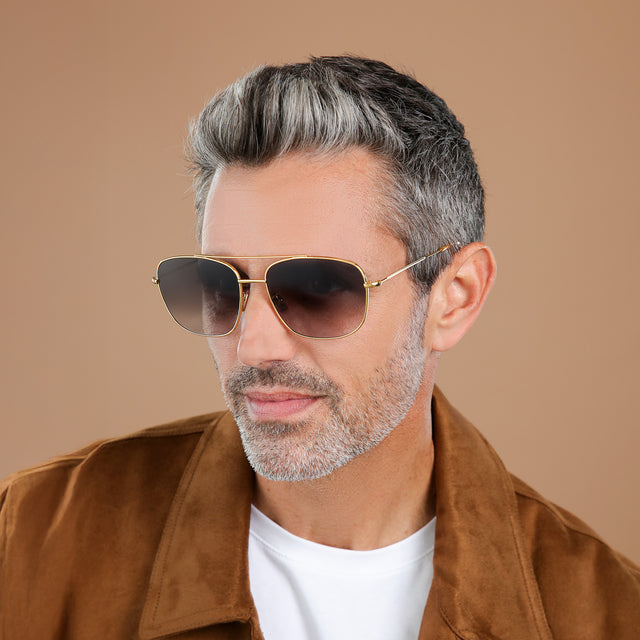 Man with salt and pepper hair and beard in a brown suede jacket wearing Frankie Sunglasses Gold with Grey Flat Gradient