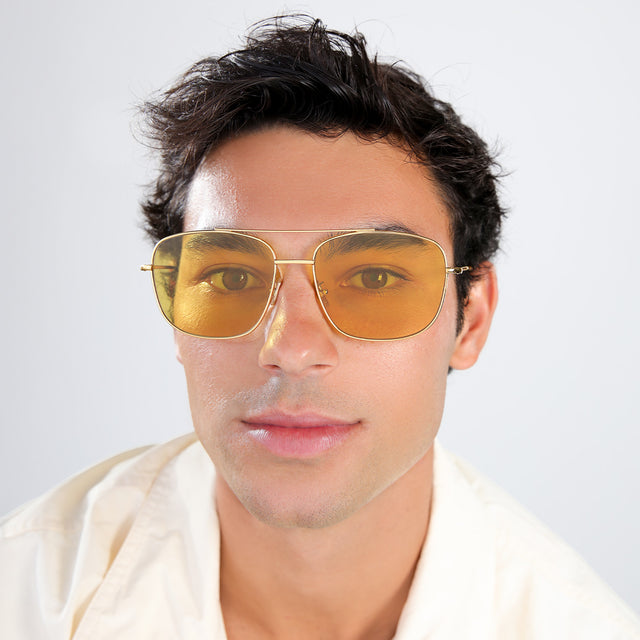 Man with brown hair in a pastel linen shirt wearing Frankie Sunglasses Gold with Honey Flat See Through