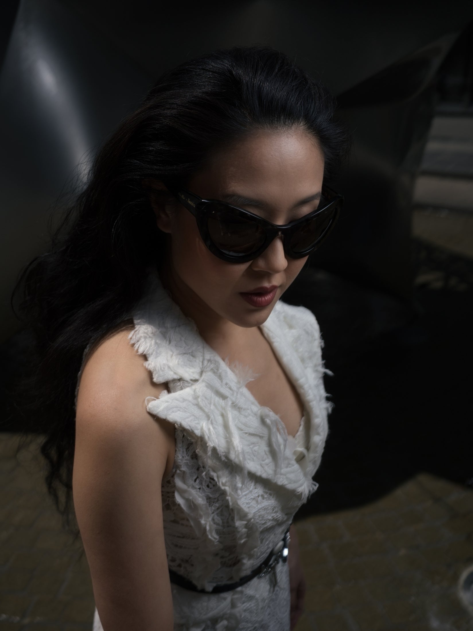 Designer wearing Kim Shui x illesteva sunglasses and a white dress while walking in a dark New York street