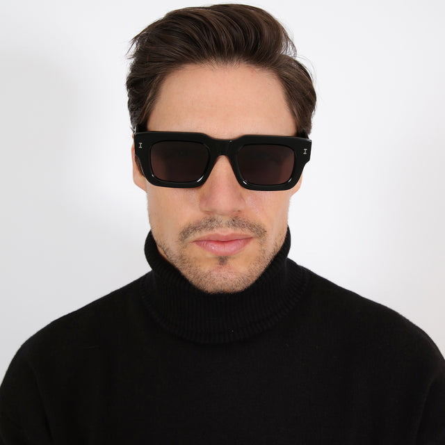 Model with short brown hair in a black turtleneck wearing Lewis 50 Sunglasses Black with Grey Flat