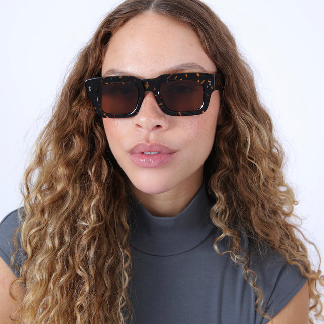 Brunette model with wavy hair in a gray mockneck wearing Lewis 50 Sunglasses Flame with Brown Flat
