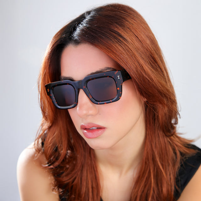 Another angle of woman with red hair in a black blouse Lewis 50 Sunglasses side view in Flame / Brown Flat