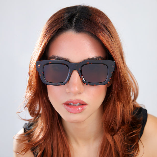 Close up of woman with red hair in a black blouse Lewis 50 Sunglasses side view in Flame / Brown Flat