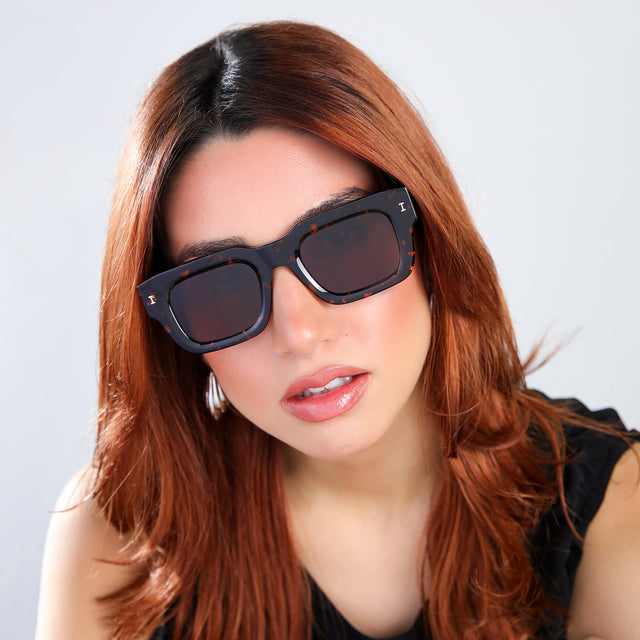 Woman with red hair in a black blouse tilting her head Lewis 50 Sunglasses side view in Flame / Brown Flat