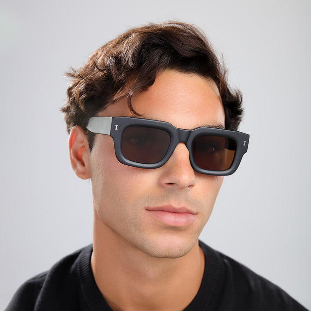 Man with brown hair in a brown shirt wearing Lewis 50 Sunglasses Matte Black with Brown Flat