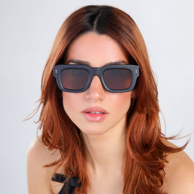 Woman with red hair in a black blouse Lewis 50 Sunglasses side view in Matte Black / Brown Flat