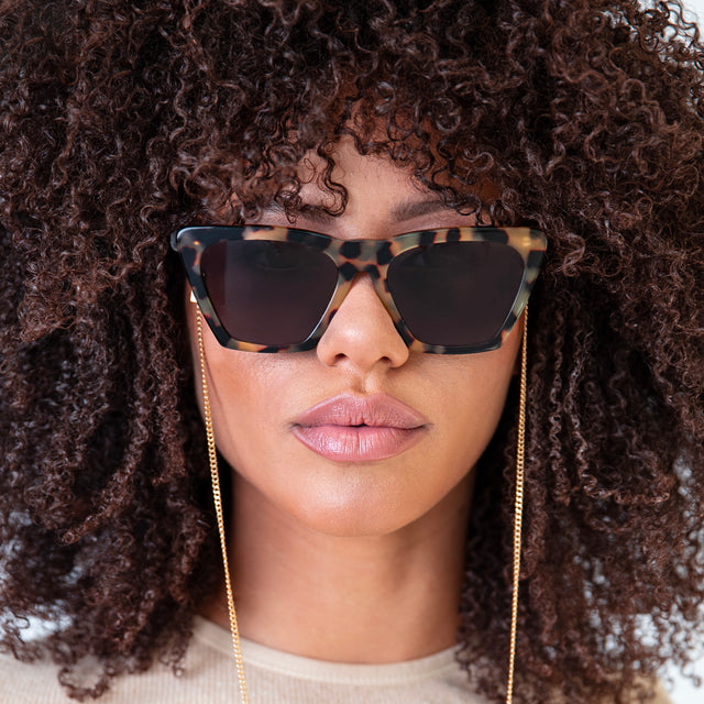 Brunette model with small, tight curls wearing Lisbon Sunglasses Tortoise with Grey