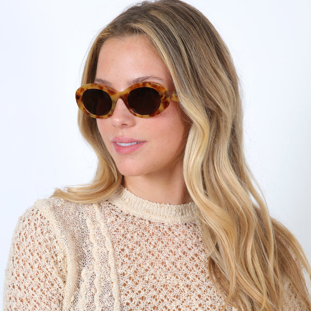 Blonde model with loose curls wearing Luna Sunglasses Amber with Brown Flat