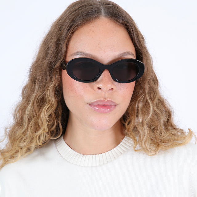 Brunette model in a white crewneck wearing Luna Sunglasses Black with Grey Flat
