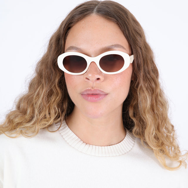 Brunette model in a white crewneck wearing Luna Sunglasses Cream with Brown Flat Gradient