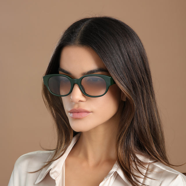 Brunette model in a cream silk blouse wearing Montreal E Sunglasses Evergreen with Taupe Flat Gradient