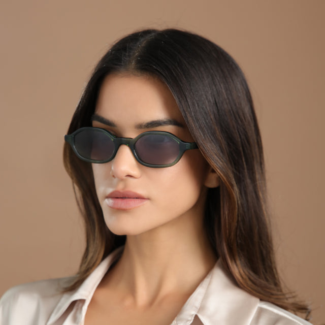 Angled portrait of brunette model in a cream silk blouse wearing Munich Sunglasses Pine with Grey Flat Gradient