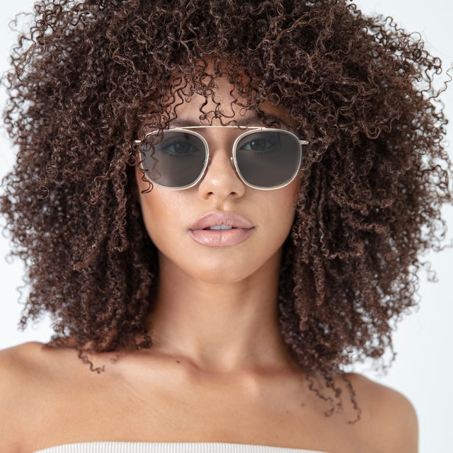 Brunette model with natural curly hair wearing Mykonos Ace Sunglasses Clear Gold with Olive Flat