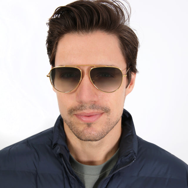 Model with short brown hair in a navy puffer jacket wearing Naxos 58 Sunglasses Gold with Olive Flat Gradient