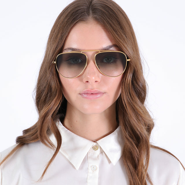 Brunette model with curled hair in a white collared blouse wearing Naxos 58 Sunglasses Gold with Olive Flat Gradient