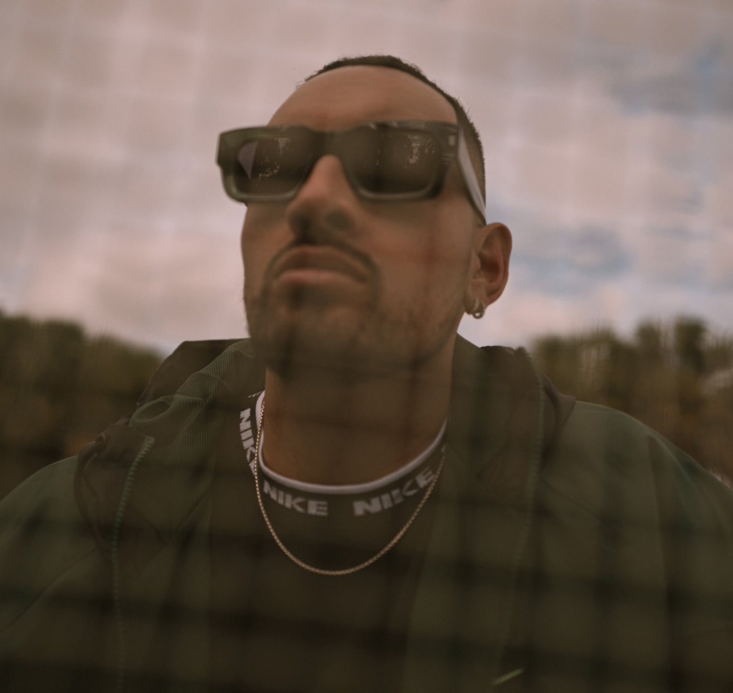 View of Nick Kyrgios through a mesh fence wearing Nick Kyrgios x illesteva Sunglasses in Pine