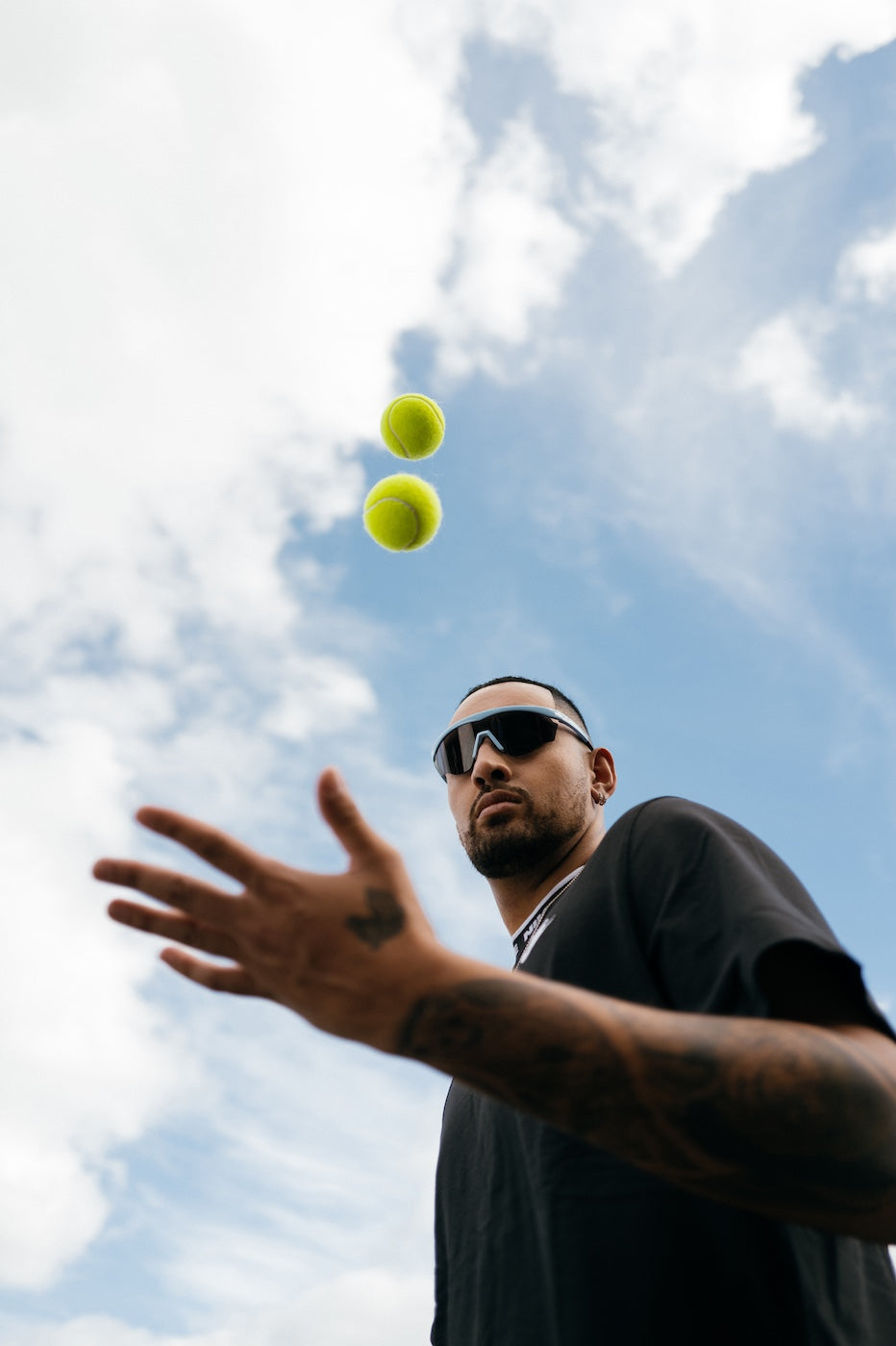 Nick Kyrgios tossing two tennis balls outdoors wearing Nick Kyrgios x illesteva Sports Frames in Baby Blue
