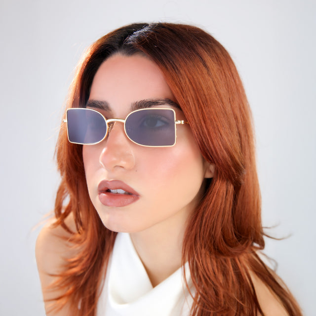 Another angle of the woman with red hair in a white blouse wearing Nostrand Sunglasses Gold with Grey