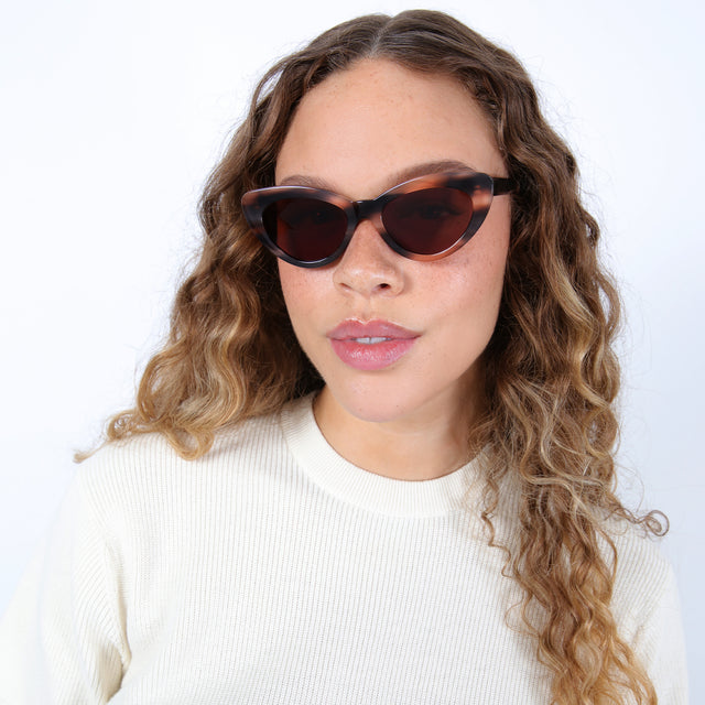 Brunette model with ombré curls wearing Pamela Sunglasses Hazelnut with Brown Flat
