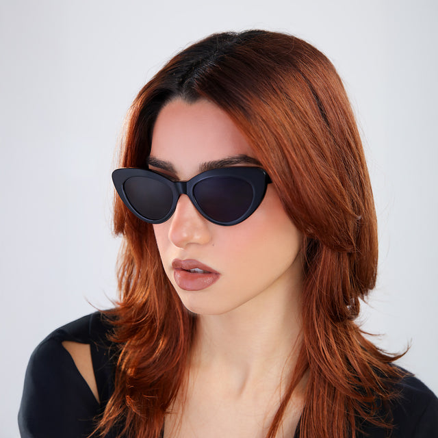 Another angle of woman with red hair in a black blouse wearing Pamela Sunglasses Black with Grey Flat