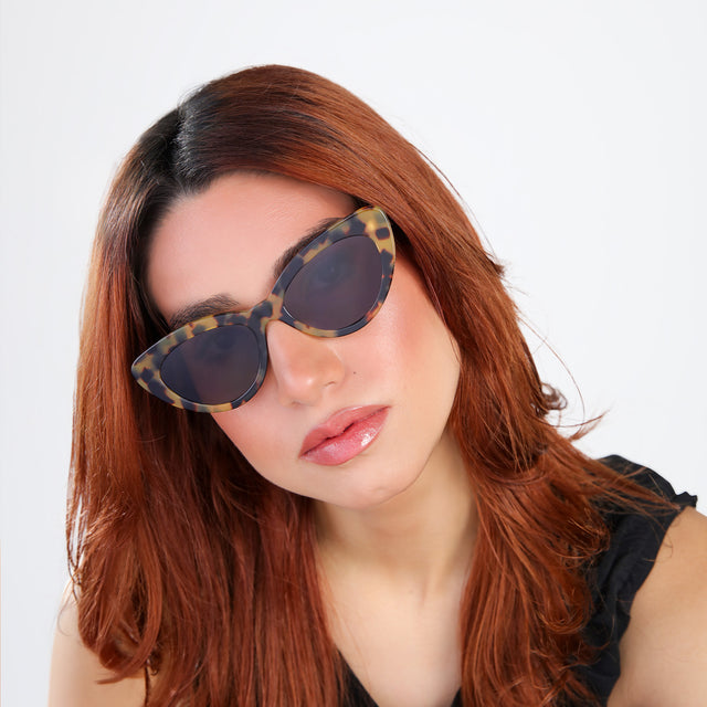 Woman with red hair in a black blouse tilting her head while wearing Pamela Sunglasses Tortoise with Grey Flat