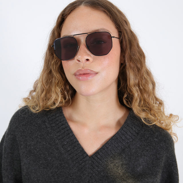 Brunette model with wavy, ombré hair wearing Patmos 58 Sunglasses Black with Grey Flat