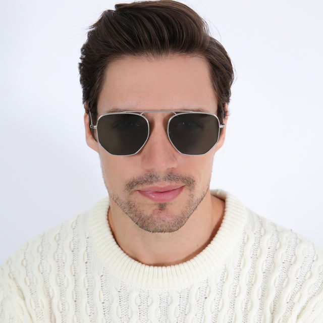 Model with brown hair combed back in a white knitted sweater wearing Patmos 58 Sunglasses Silver with Olive Flat