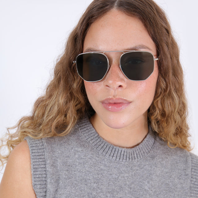 Brunette model with wavy, ombré hair wearing Patmos 58 Sunglasses Silver with Olive Flat