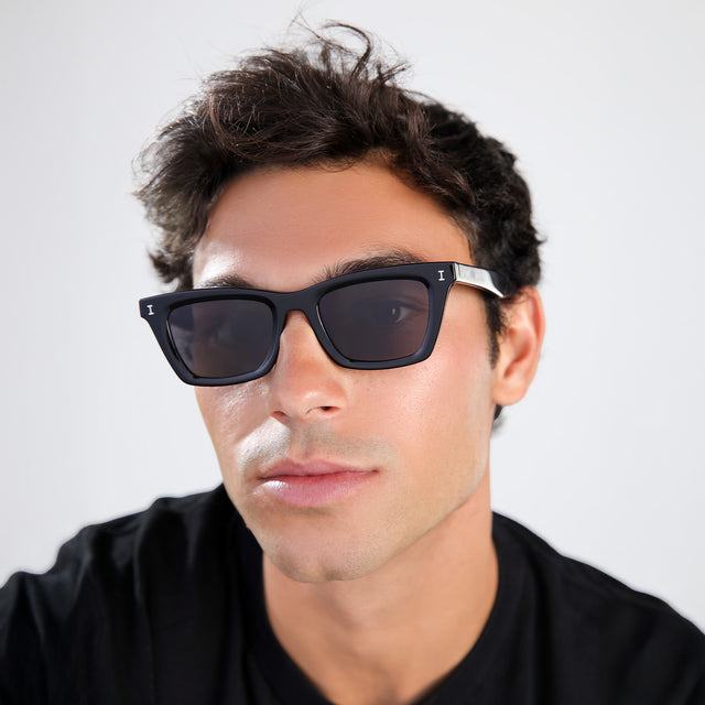 Man with brown hair in a black shirt wearing Portugal Sunglasses Black with Grey Flat